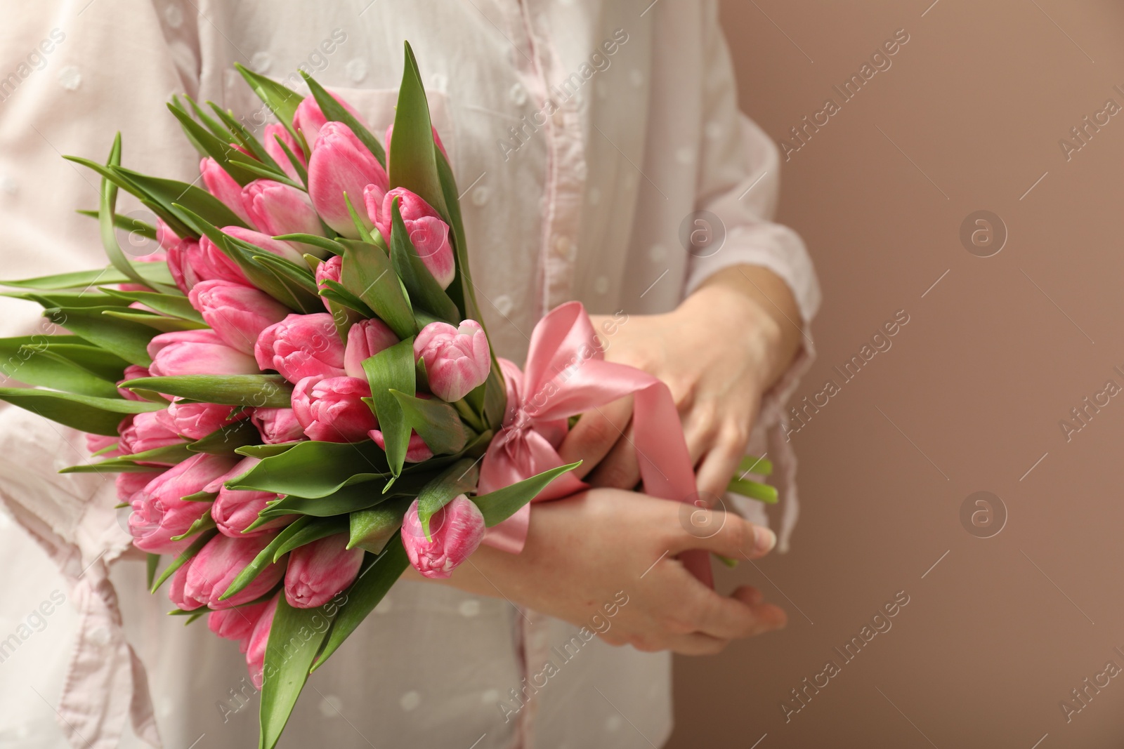 Photo of Woman with bouquet of beautiful tulips on dark beige background, closeup. Space for text