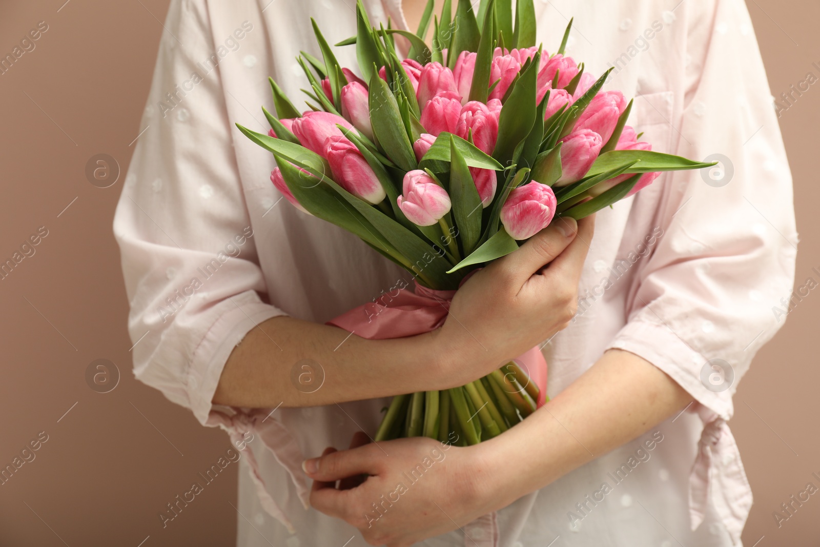 Photo of Woman with bouquet of beautiful tulips on dark beige background, closeup