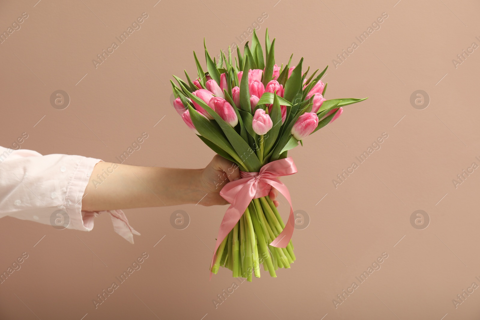 Photo of Woman with bouquet of beautiful tulips on dark beige background, closeup