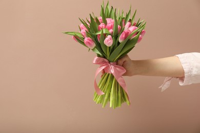 Photo of Woman with bouquet of beautiful tulips on dark beige background, closeup. Space for text