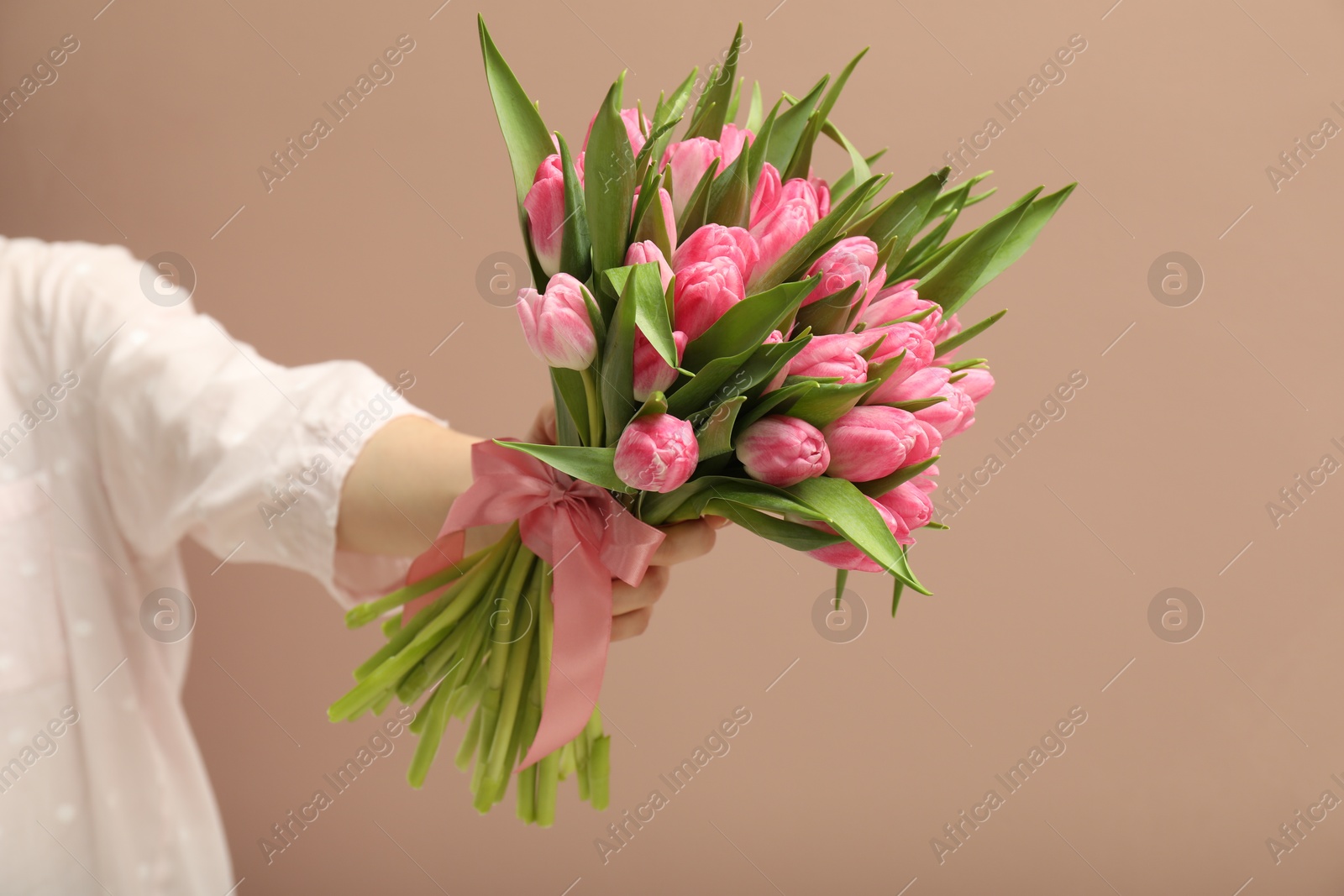 Photo of Woman with bouquet of beautiful tulips on dark beige background, closeup