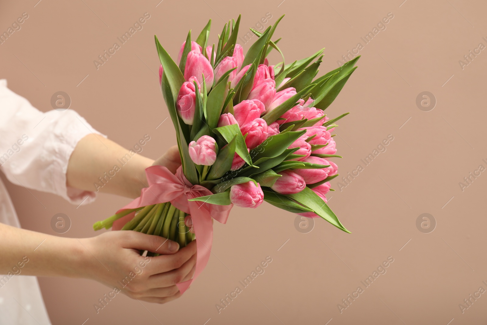 Photo of Woman with bouquet of beautiful tulips on dark beige background, closeup