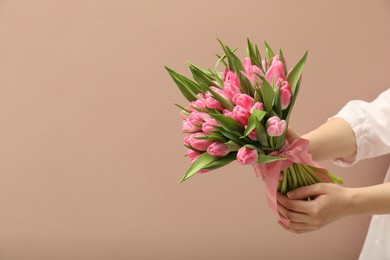 Photo of Woman with bouquet of beautiful tulips on dark beige background, closeup. Space for text