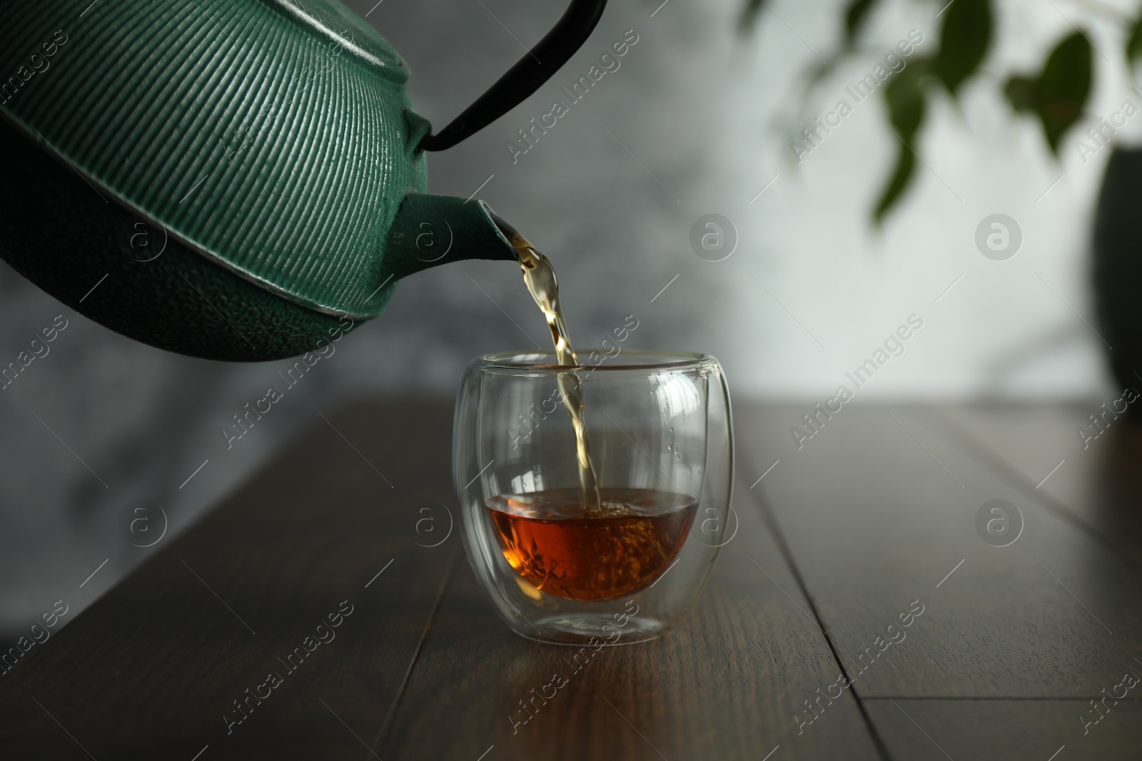 Pouring freshly brewed tea from teapot into cup at wooden table, closeup Photo of Pouring freshly brewed tea from teapot into cup at wooden table, closeup