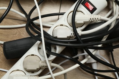 Photo of Extension power boards overloaded with plugs on wooden floor, closeup