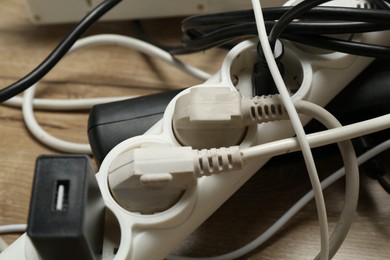 Photo of Extension power boards overloaded with plugs on wooden floor, closeup