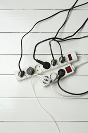 Photo of Extension power boards overloaded with plugs on wooden floor, top view