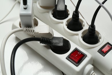 Photo of Extension power boards overloaded with plugs on wooden floor, closeup