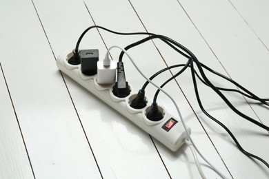 Photo of Extension power board overloaded with plugs on white wooden floor