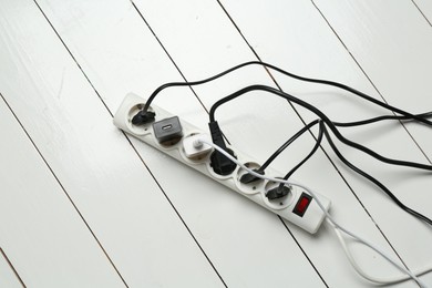 Photo of Extension power board overloaded with plugs on white wooden floor, top view