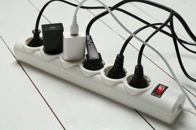 Photo of Extension power board overloaded with plugs on white wooden floor, closeup