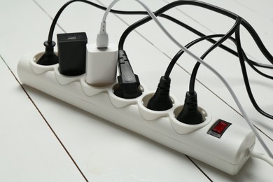 Photo of Extension power board overloaded with plugs on white wooden floor, closeup