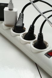 Photo of Extension power board overloaded with plugs on white wooden floor, closeup