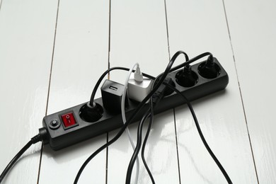 Photo of Extension power board overloaded with plugs on white wooden floor