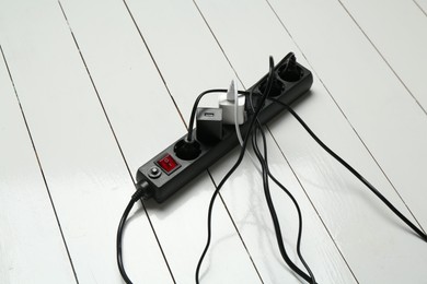 Photo of Extension power board overloaded with plugs on white wooden floor