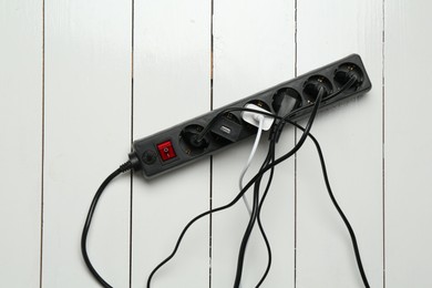 Photo of Extension power board overloaded with plugs on white wooden floor, top view