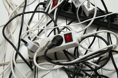 Photo of Extension power boards overloaded with plugs on wooden floor, closeup