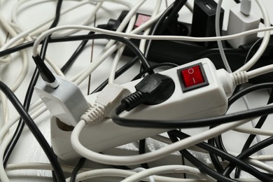 Photo of Extension power boards overloaded with plugs on wooden floor, closeup