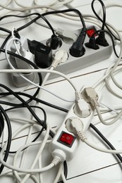 Photo of Extension power boards overloaded with plugs on wooden floor, closeup