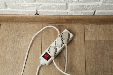 Photo of Extension power board overloaded with plugs on wooden floor, above view