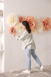 Woman decorating wall with beautiful paper flowers at home