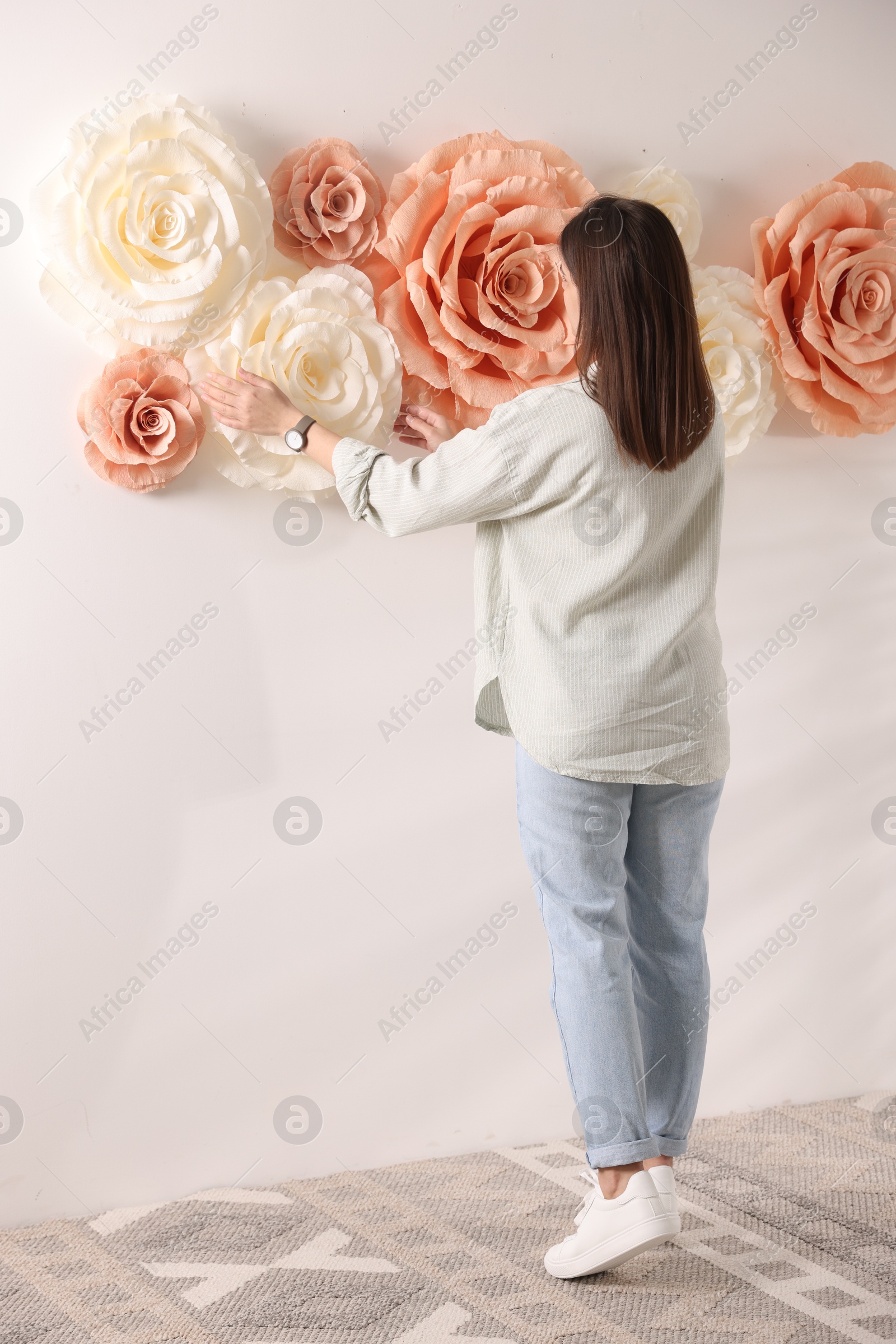 Photo of Woman decorating wall with beautiful paper flowers at home, back view