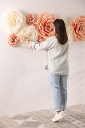 Woman decorating wall with beautiful paper flowers at home, back view