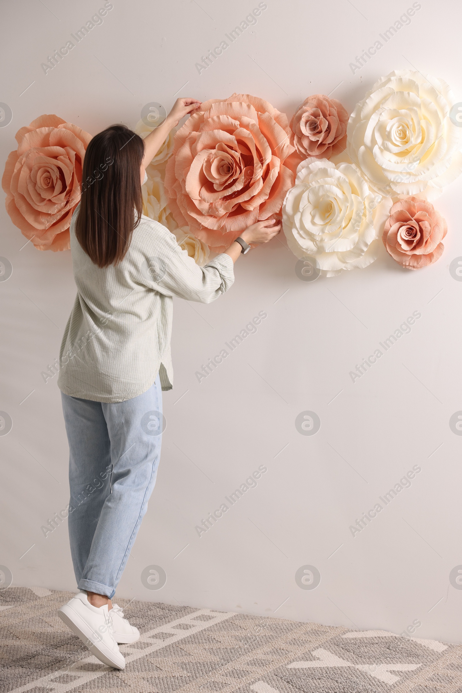 Photo of Woman decorating wall with beautiful paper flowers at home, back view