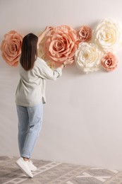 Woman decorating wall with beautiful paper flowers at home, back view