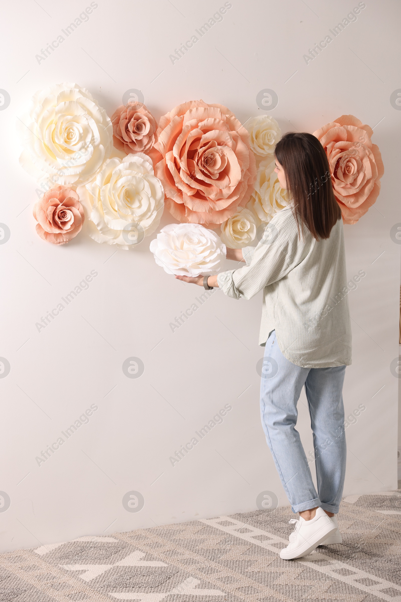 Photo of Woman decorating wall with beautiful paper flowers at home