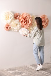 Woman decorating wall with beautiful paper flowers at home