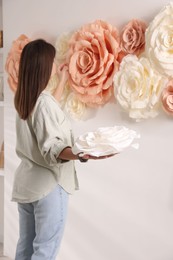 Woman decorating wall with beautiful paper flowers at home