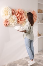 Woman decorating wall with beautiful paper flowers at home