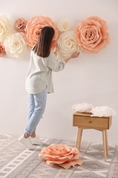 Woman decorating wall with beautiful paper flowers at home