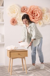 Woman decorating wall with beautiful paper flowers at home