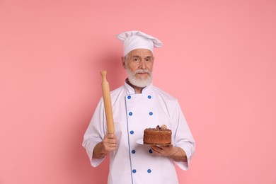 Professional pastry chef with delicious chocolate cake and rolling pin on pink background