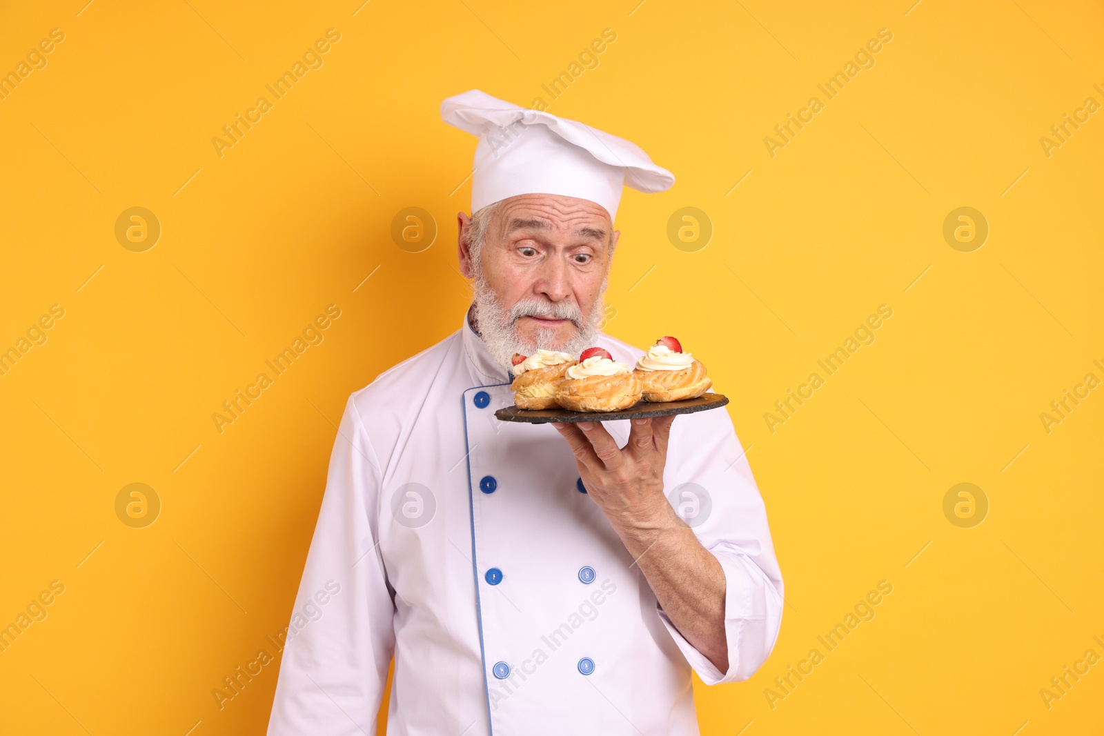 Photo of Professional pastry chef with delicious profiteroles on orange background