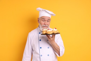 Professional pastry chef with delicious profiteroles on orange background