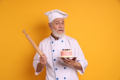 Professional pastry chef with delicious cake and rolling pin on orange background