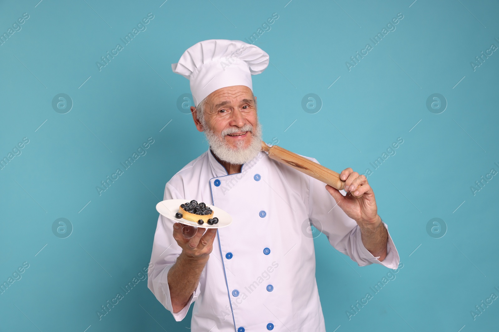 Photo of Professional pastry chef with tart and rolling pin on light blue background