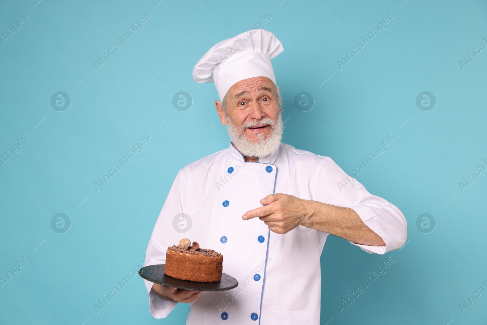 Photo of Professional pastry chef with delicious chocolate cake on light blue background