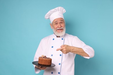 Professional pastry chef with delicious chocolate cake on light blue background