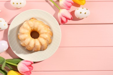 Photo of Delicious bundt cake, Easter eggs and tulips on pink wooden table, flat lay. Space for text