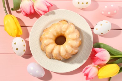 Photo of Delicious bundt cake, Easter eggs and tulips on pink wooden table, flat lay