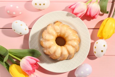 Photo of Delicious bundt cake, Easter eggs and tulips on pink wooden table, flat lay