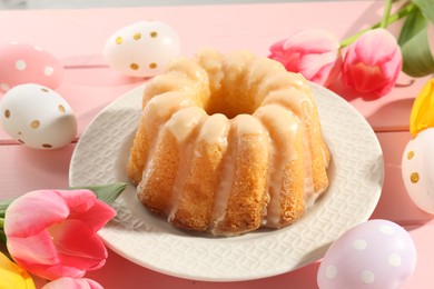 Photo of Delicious bundt cake, Easter eggs and tulips on pink wooden table, closeup