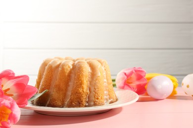 Photo of Delicious bundt cake, Easter eggs and tulips on pink wooden table, closeup