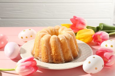 Photo of Delicious bundt cake, Easter eggs and tulips on pink wooden table, closeup