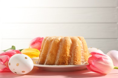 Photo of Delicious bundt cake, Easter eggs and tulips on pink wooden table, closeup