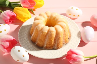 Photo of Delicious bundt cake, Easter eggs and tulips on pink wooden table, closeup